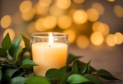 A candle burns brightly surrounded by green leaves