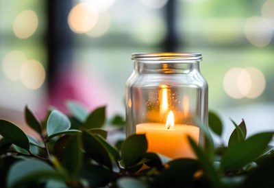 A candle glows in a jar amid lush greenery