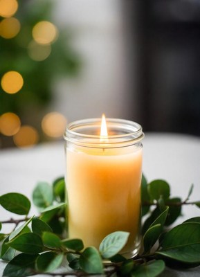 A lit candle sits on a table surrounded by greenery