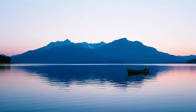 A boat rests on a lake at sunset with mountains