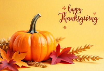 A ripe pumpkin sits on a table with fall leaves and wheat