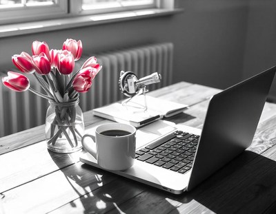 A wooden desk with a laptop, coffee, and tulips