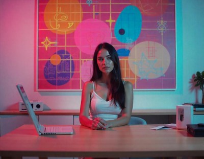 A woman sits at a desk in front of a colorful painting