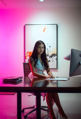 A woman works at a desk in a pink-lit room