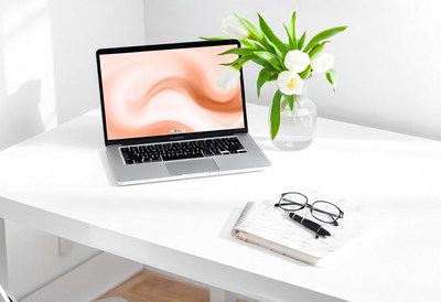 A laptop, notebook, and glasses sit on a desk with flowers
