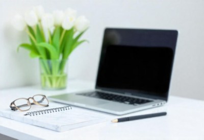 Notebook, glasses, pen, laptop, and tulips on desk