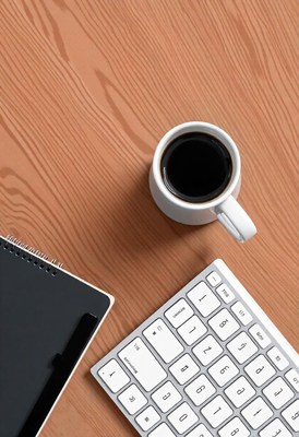 A cup of coffee sits on a wooden desk next to a keyboard
