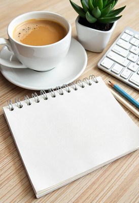 A blank notepad sits on a desk with coffee and a keyboard