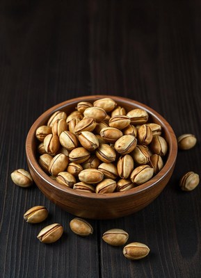 A bowl of pistachios on a dark wood table