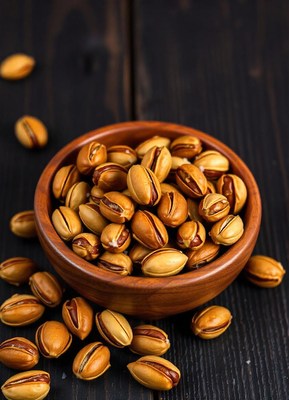 A bowl of roasted pistachios sits on a dark wooden surface