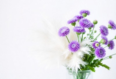 Purple flowers and white feathers sit in a vase
