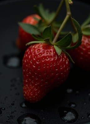 A juicy red strawberry with green leaves on a black surface