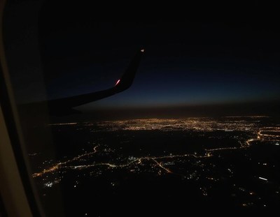 A city lights up the night sky from a plane window