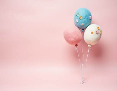 Three pastel balloons float against a pink background