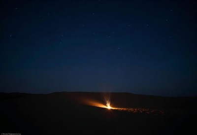 Campfire flickering under a starry night sky