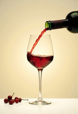 Red wine pouring into a glass with cherries on the side