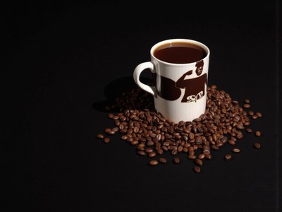 Coffee cup surrounded by roasted beans on black surface