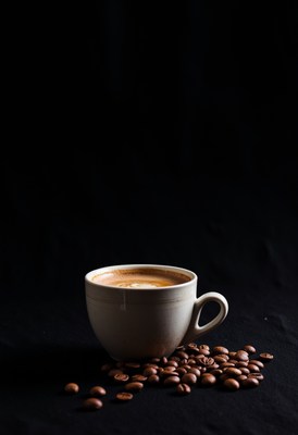 Warm cup of coffee beside scattered coffee beans