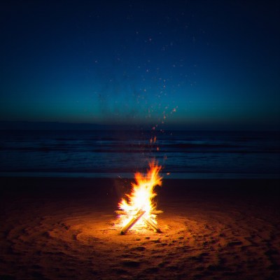 Fire burns brightly on the quiet beach at dusk