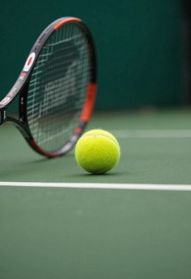 Tennis ball and racket on green court surface in play