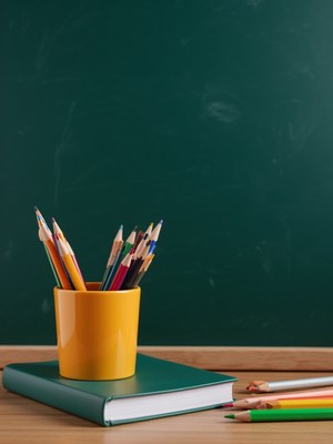Colored pencils in a yellow cup beside a green notebook