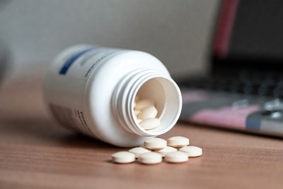 Pills spilled on a wooden table near a laptop