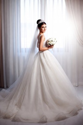 Bride in elegant gown with bouquet standing by window