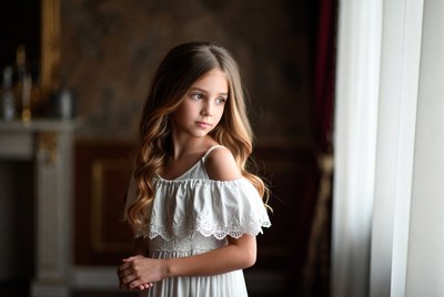 Young girl in white dress looks out window