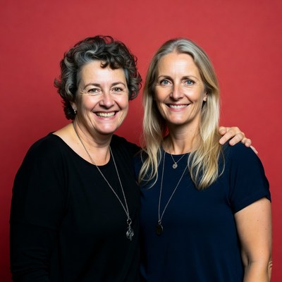Two women pose together against a red background