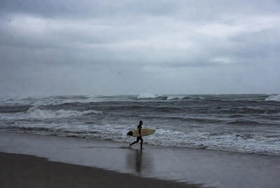 Surfer runs towards ocean during cloudy day
