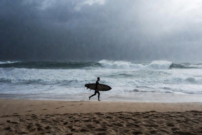 Surfer walks along the beach during rain