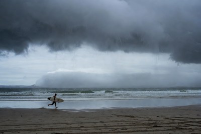 Surfer runs on beach before storm