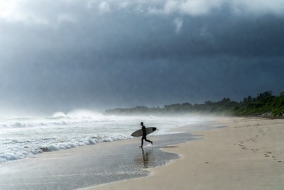 Surfer walks along dark beach before storm