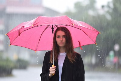 Girl standing under pink umbrella in rain