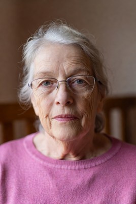 Elderly woman sitting indoors with glasses