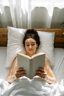 Nude woman reading book in bed