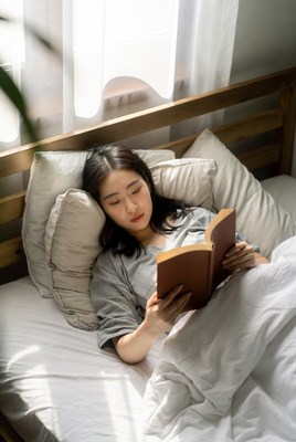 Asian woman reading book in bed