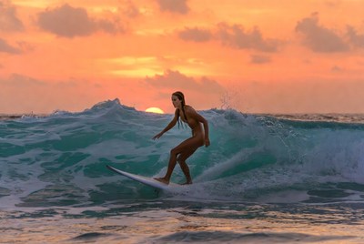 Surfer rides wave at sunset