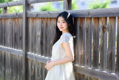 Young woman stands by wooden fence