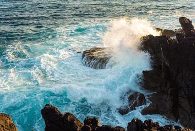 Waves crash on rocky shoreline in sunlight
