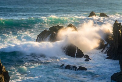 Waves crash over rocky coastline at sunset