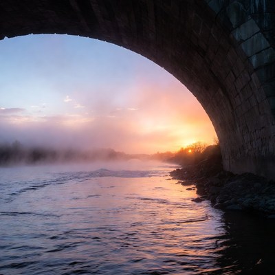 Sunrise over river under bridge