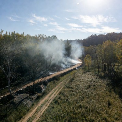 Smoke rising from dirt road near trees