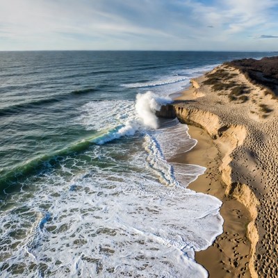Waves crash on sandy shore near cliffs