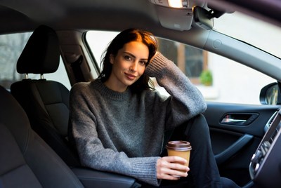 Woman sits in car with coffee
