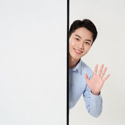 Young man greeting from behind wall