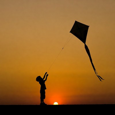 Child flying kite at sunset