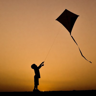 Child flying kite at sunset