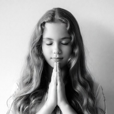 Girl with hands clasped in prayer indoors