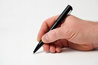 Hand holding a black pen on white paper